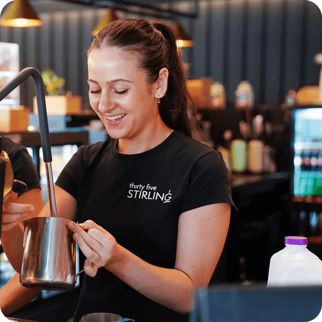 Friendly barista at Thirty Five Stirling café in Thebarton, Adelaide, preparing coffee with a smile behind the counter.