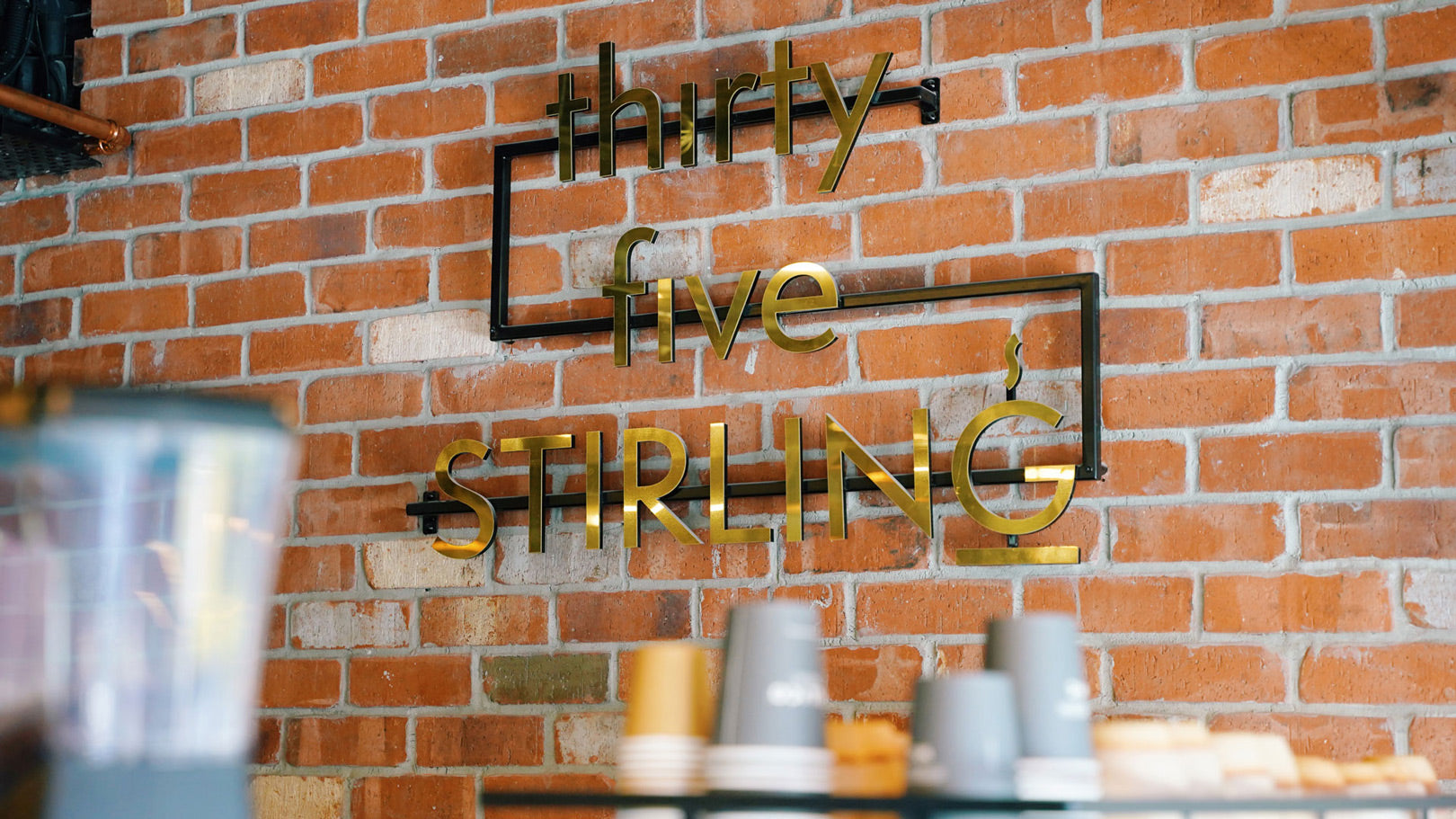Thirty Five Stirling café gold logo on exposed brick wall inside heritage building in Thebarton, Adelaide – blending modern café style with historic character.